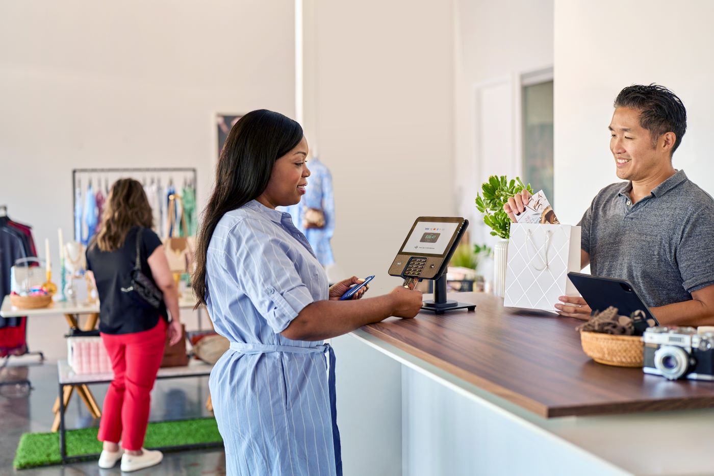 Woman making a payment with a card at a retail store counter while cashier places items in a shopping bag.